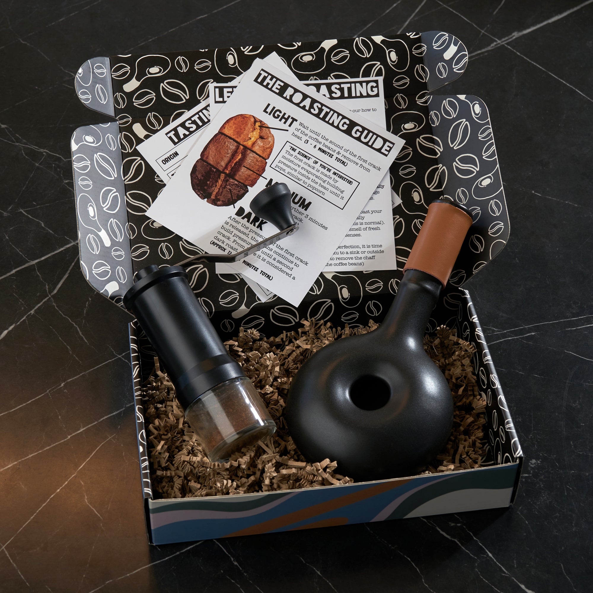 Coffee grinder and scoop set with a roasting guide in a box on a dark surface