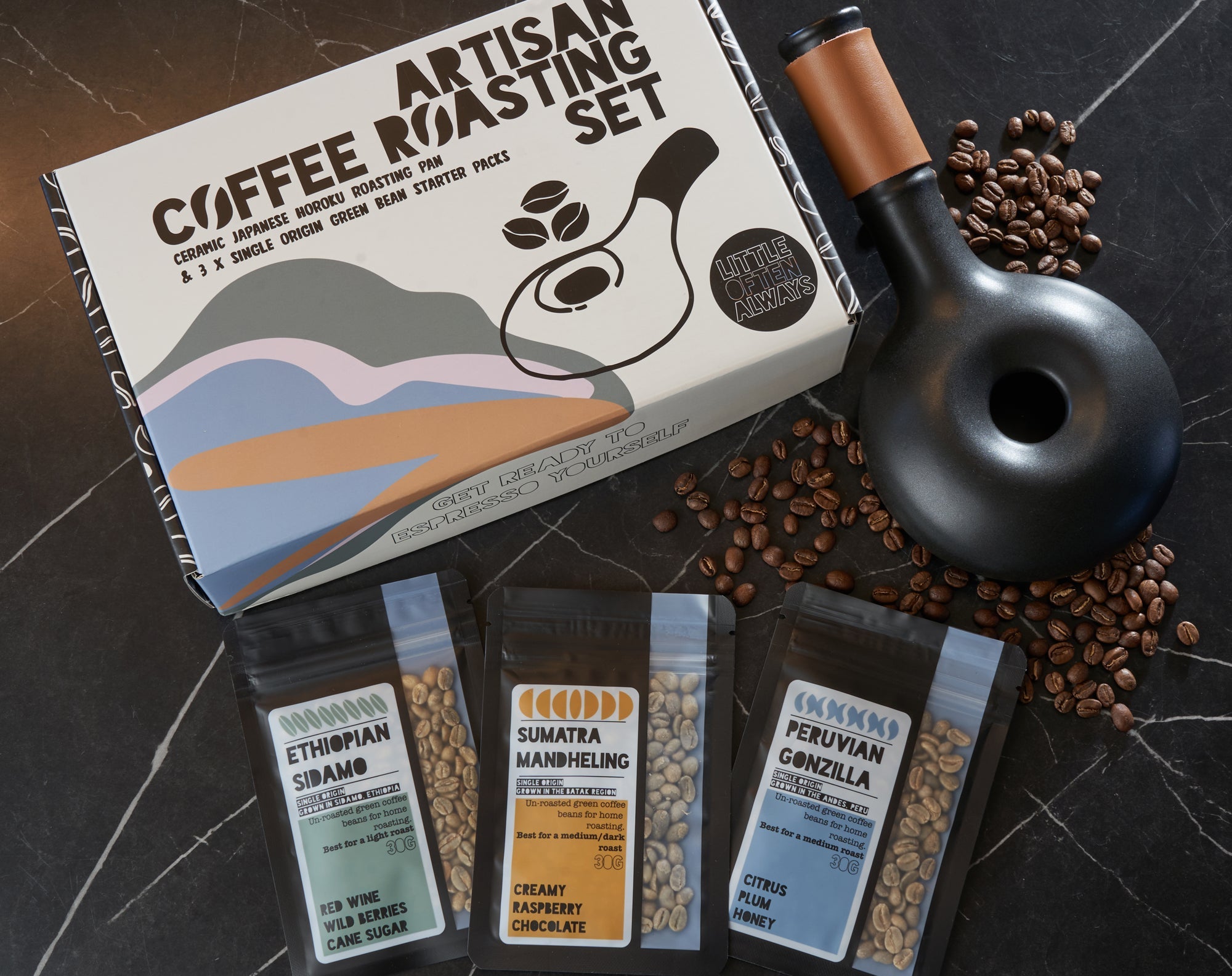 Artisan coffee roasting set with packaging, coffee beans, and a roasting tool on a dark surface.
