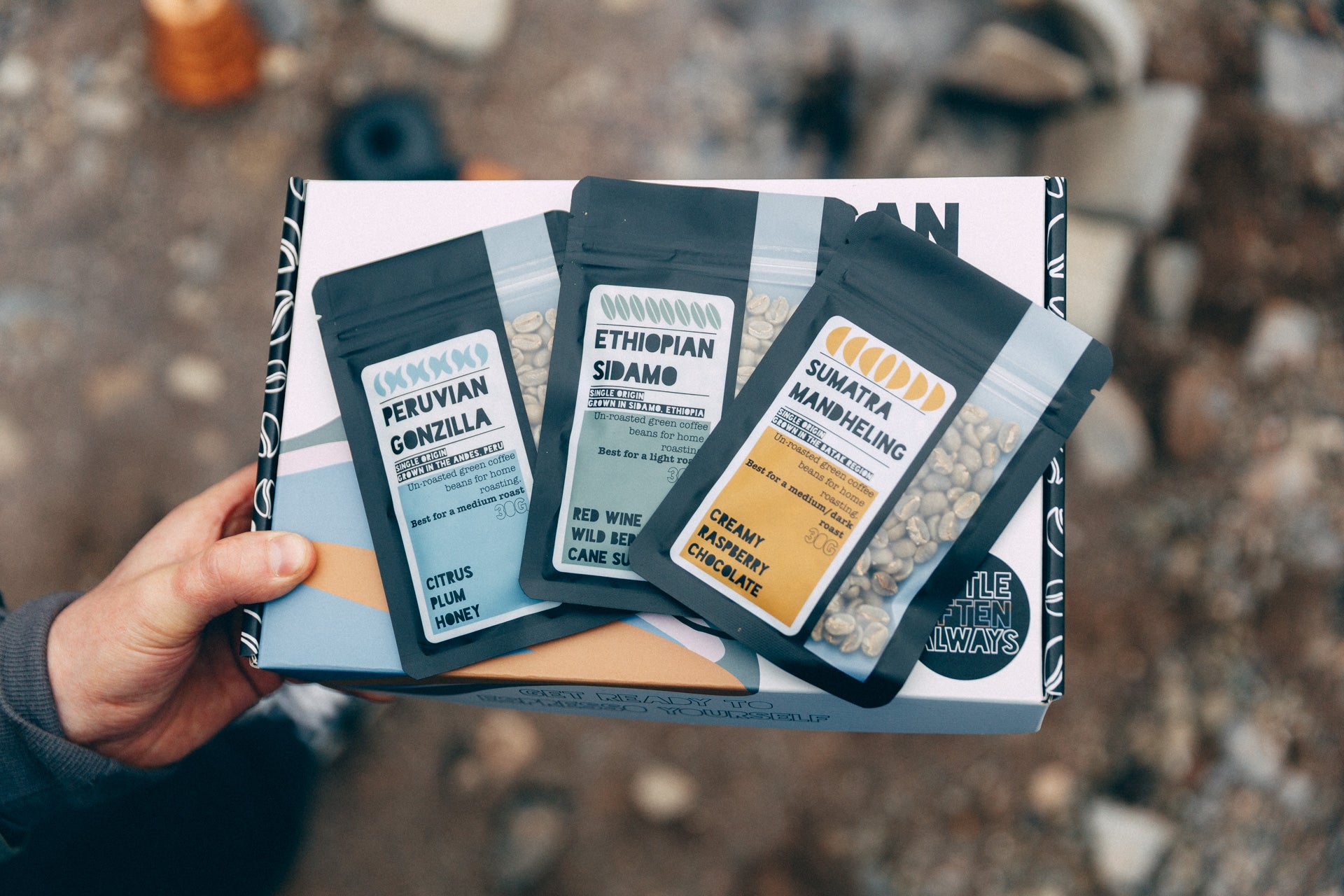 Hand holding a box of coffee packages with visible branding on a blurred natural background