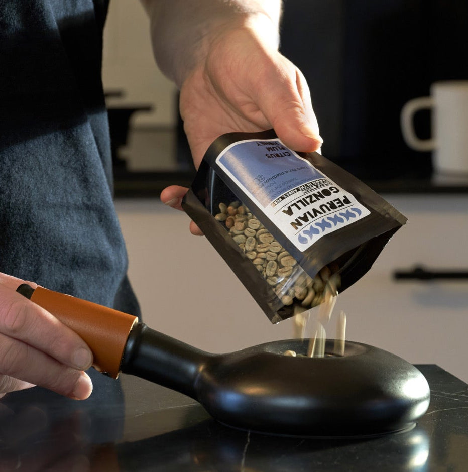 Person pouring coffee beans from a package into a black scoop on a kitchen counter.