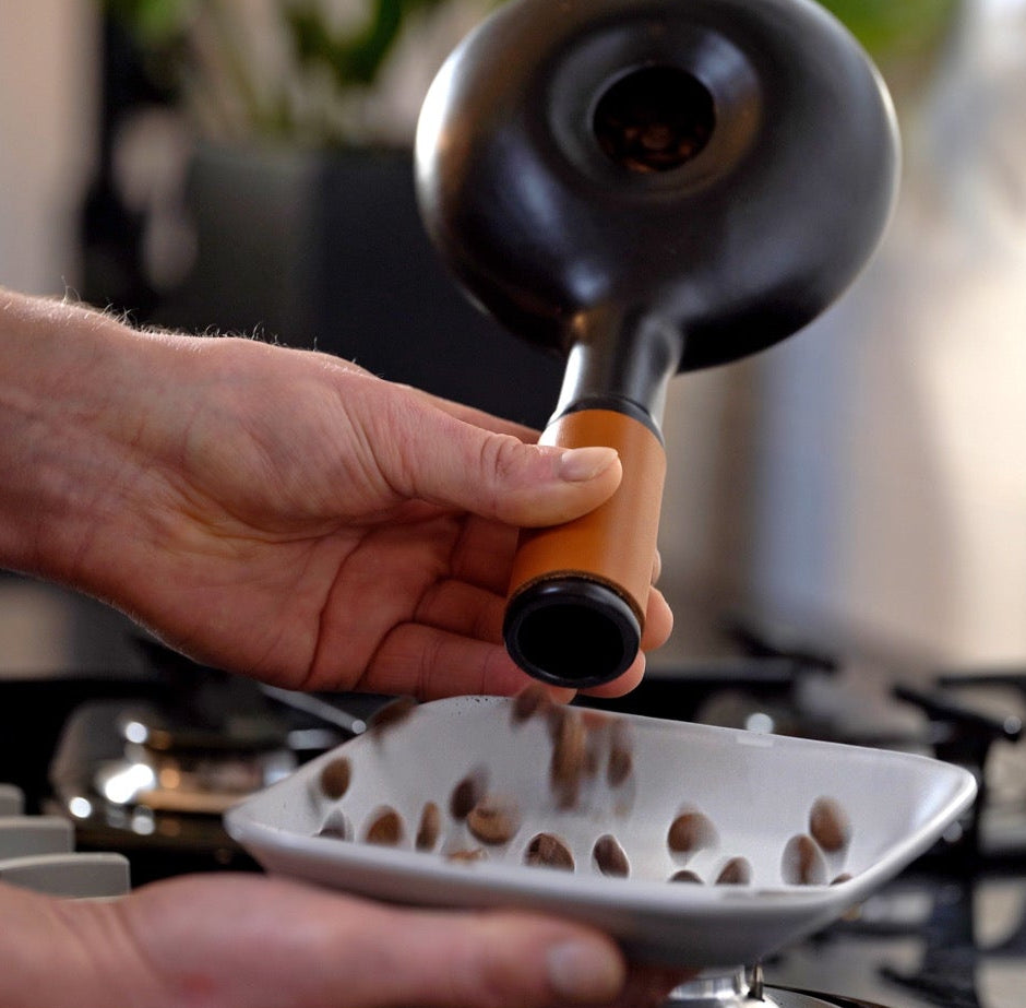 Person using a coffee scoop to transfer coffee beans into a white container.