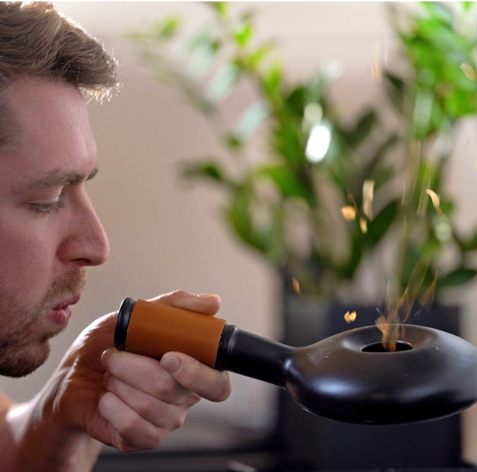 Man using a handheld incense burner with smoke in a blurred indoor setting